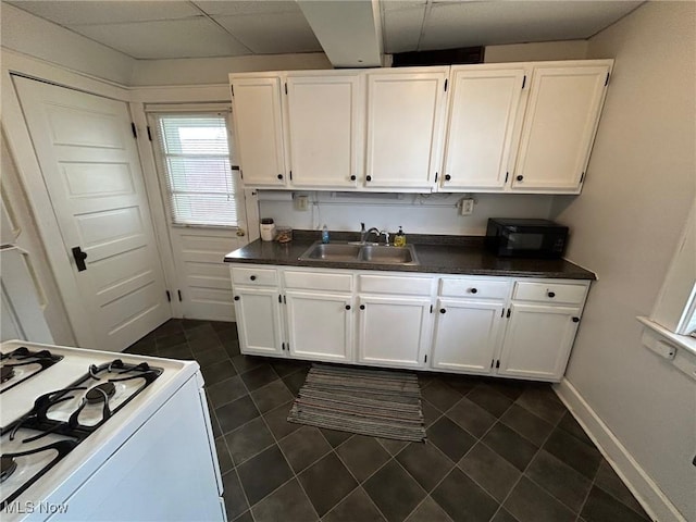 kitchen with dark countertops, white range with gas stovetop, white cabinets, and a sink