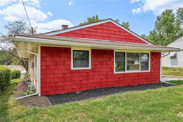 view of property exterior with a shingled roof and a yard