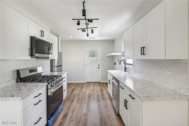 kitchen featuring rail lighting, stainless steel appliances, light wood-type flooring, white cabinetry, and a sink