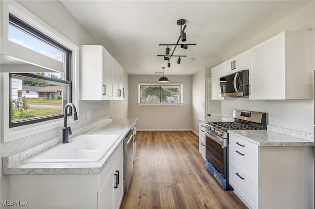 kitchen featuring pendant lighting, light countertops, appliances with stainless steel finishes, white cabinetry, and a sink