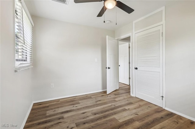 unfurnished bedroom with wood finished floors, visible vents, a ceiling fan, baseboards, and a closet