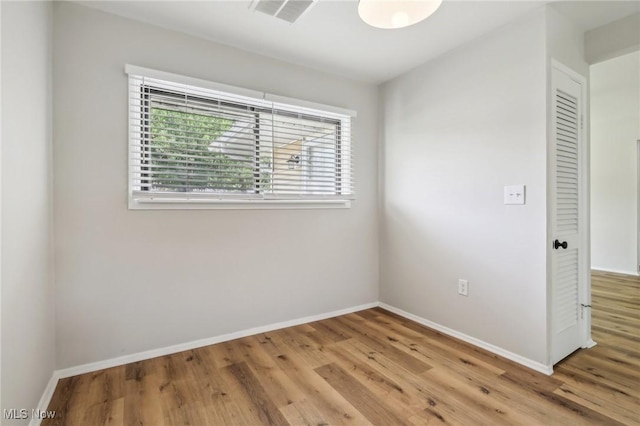 spare room featuring light wood-type flooring, visible vents, and baseboards