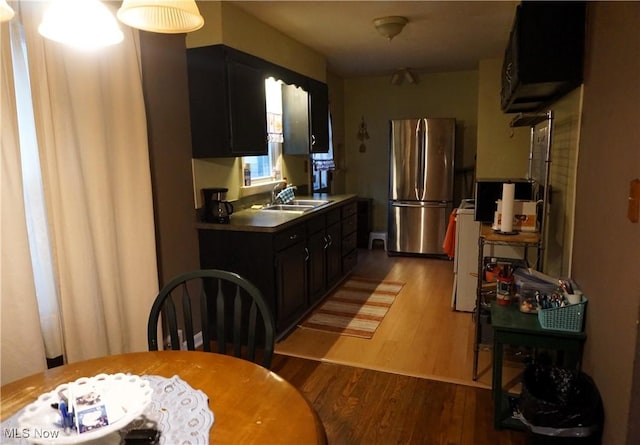 kitchen featuring wood finished floors, a sink, freestanding refrigerator, and dark cabinetry