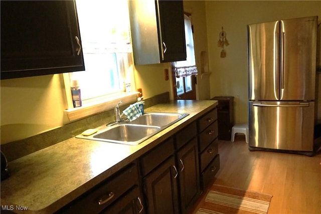 kitchen featuring freestanding refrigerator, a sink, light wood finished floors, and dark brown cabinets