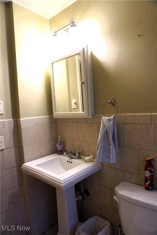 half bath with wainscoting, toilet, and tile walls