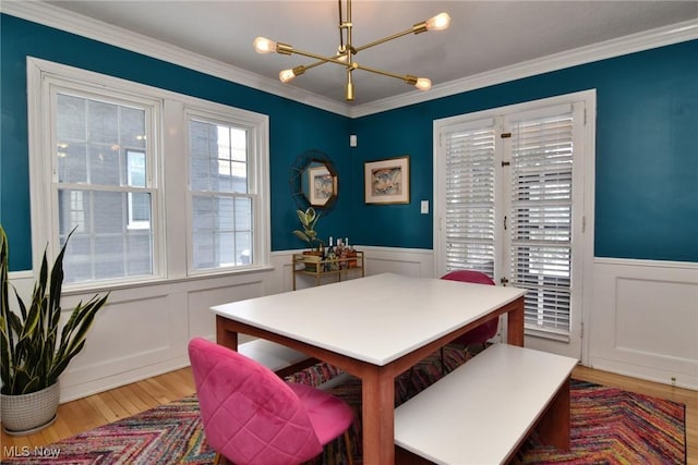 dining area featuring ornamental molding, wainscoting, a notable chandelier, and wood finished floors