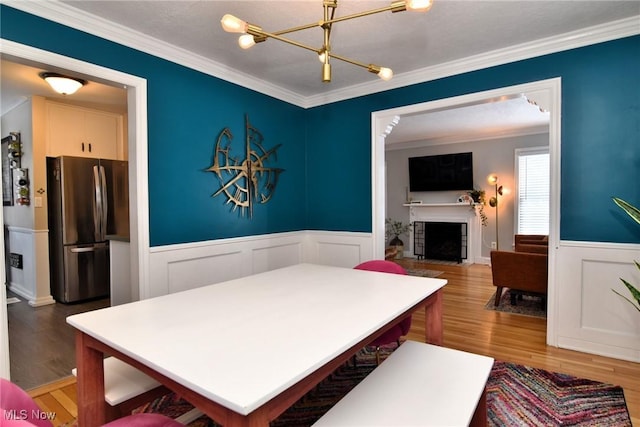 dining area featuring a fireplace with flush hearth, ornamental molding, wainscoting, and wood finished floors