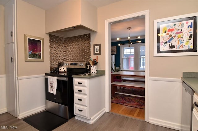 kitchen featuring electric range, decorative backsplash, white cabinets, wood finished floors, and premium range hood