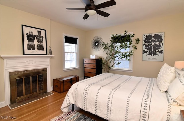 bedroom with a ceiling fan, wood finished floors, and a glass covered fireplace