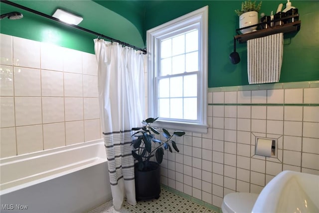 full bath with wainscoting, toilet, tile patterned flooring, shower / bath combo with shower curtain, and tile walls