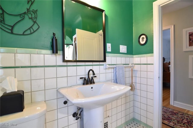 half bathroom featuring toilet, tile walls, and a sink