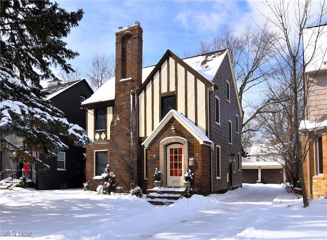 tudor home with brick siding, a chimney, and stucco siding