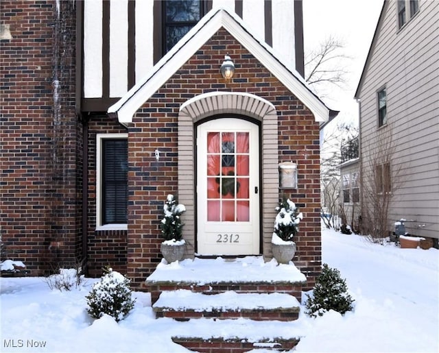 snow covered property entrance with brick siding