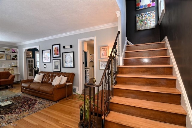 stairs with visible vents, a textured ceiling, ornamental molding, and wood finished floors