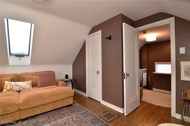 sitting room featuring vaulted ceiling with skylight, visible vents, baseboards, and wood finished floors