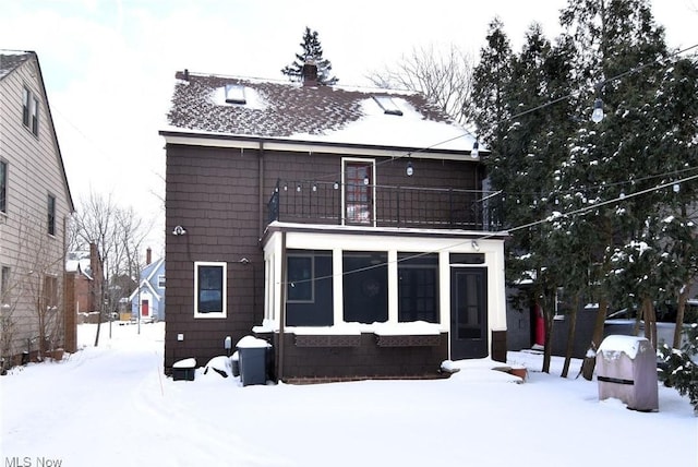 snow covered back of property with a sunroom and a balcony