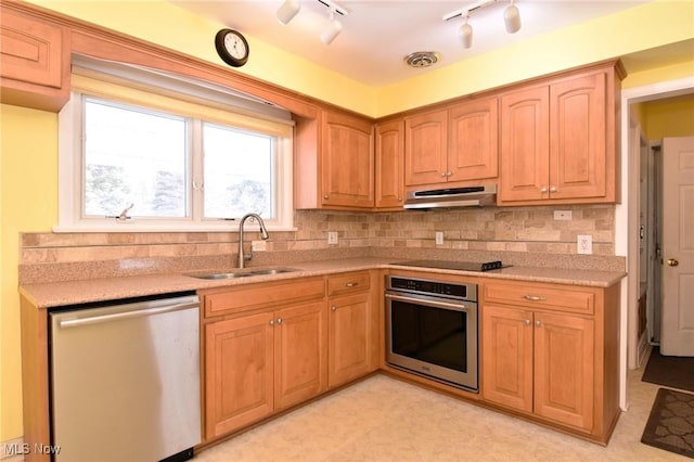 kitchen with under cabinet range hood, a sink, light countertops, appliances with stainless steel finishes, and decorative backsplash