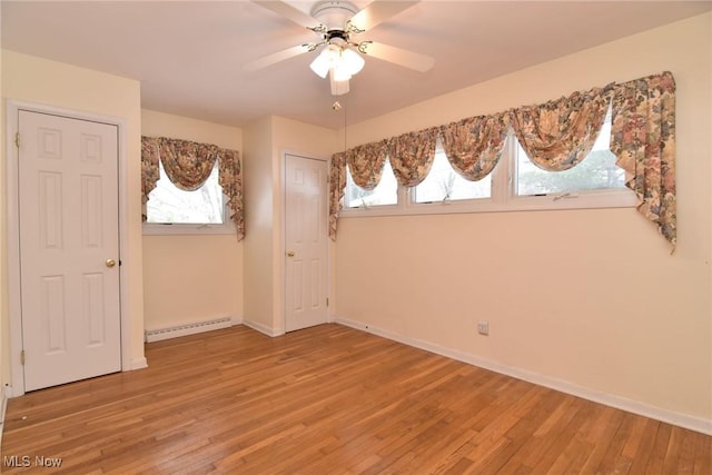 interior space with baseboard heating, wood finished floors, a ceiling fan, and baseboards