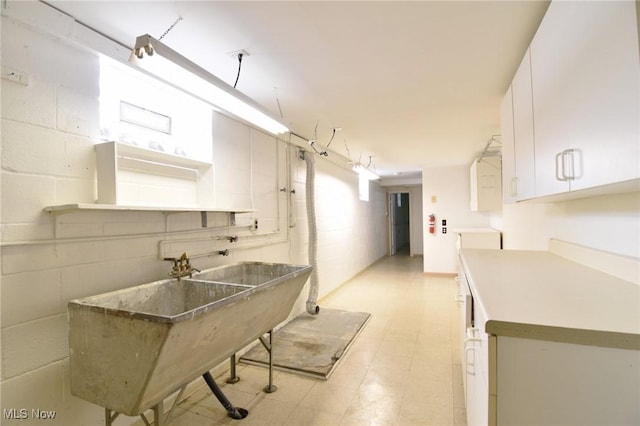 kitchen with light floors, a sink, concrete block wall, and white cabinets