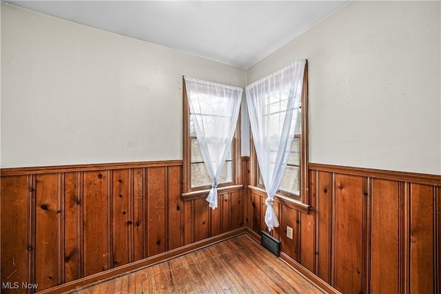 unfurnished room with a healthy amount of sunlight, wainscoting, and wood-type flooring