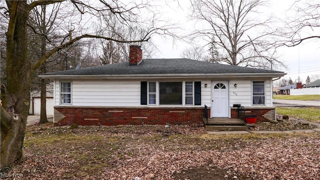 bungalow with a shingled roof, brick siding, and a chimney