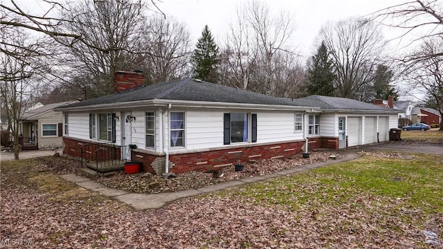 ranch-style house with brick siding, roof with shingles, a chimney, an attached garage, and driveway