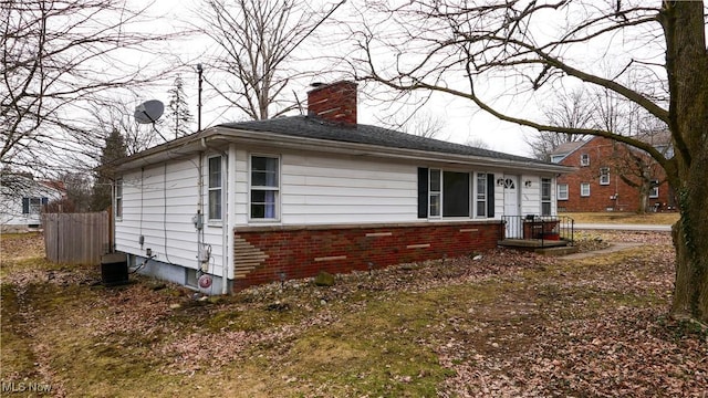 view of home's exterior with cooling unit, brick siding, fence, and a chimney