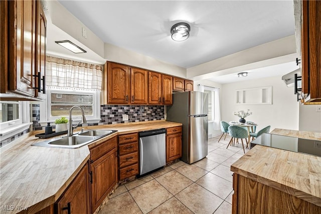 kitchen featuring light tile patterned floors, stainless steel appliances, a sink, brown cabinets, and tasteful backsplash