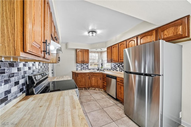 kitchen with light countertops, appliances with stainless steel finishes, light tile patterned flooring, a sink, and under cabinet range hood