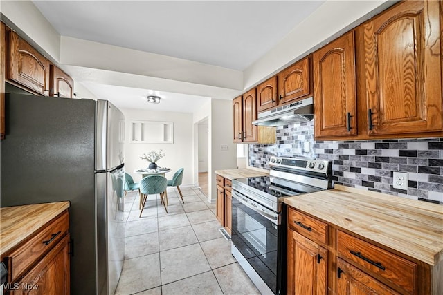 kitchen featuring light tile patterned floors, decorative backsplash, brown cabinetry, stainless steel appliances, and under cabinet range hood