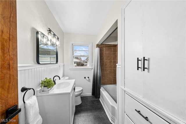 bathroom featuring wainscoting, vanity, toilet, and shower / bath combo with shower curtain