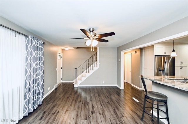 kitchen with stainless steel fridge, ceiling fan, light stone countertops, dark wood finished floors, and baseboards