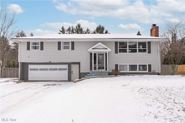 split foyer home with a garage, fence, and a chimney