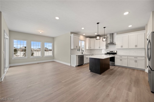 kitchen featuring wall chimney exhaust hood, appliances with stainless steel finishes, light countertops, and white cabinetry