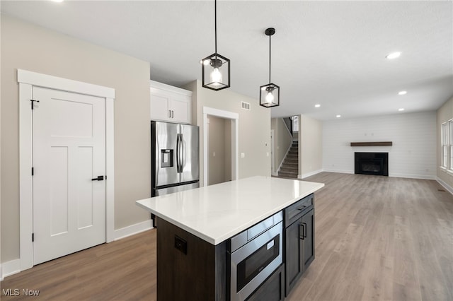 kitchen with white cabinets, stainless steel appliances, light countertops, a fireplace, and pendant lighting