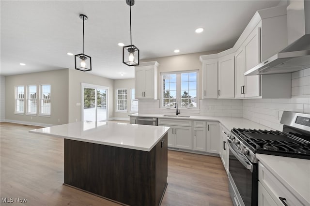 kitchen with wall chimney exhaust hood, stainless steel appliances, light countertops, and a sink