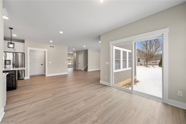 unfurnished living room featuring recessed lighting, visible vents, baseboards, stairs, and light wood-type flooring