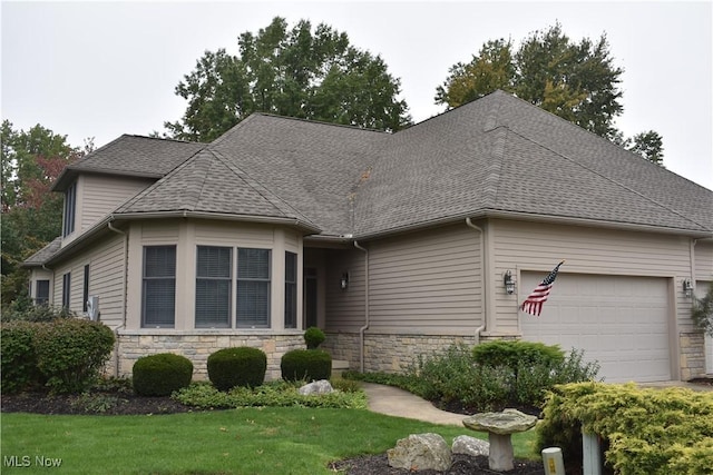 view of front facade with an attached garage, stone siding, and roof with shingles