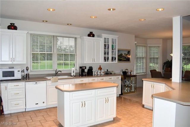kitchen with white appliances, a kitchen island, glass insert cabinets, white cabinetry, and a sink