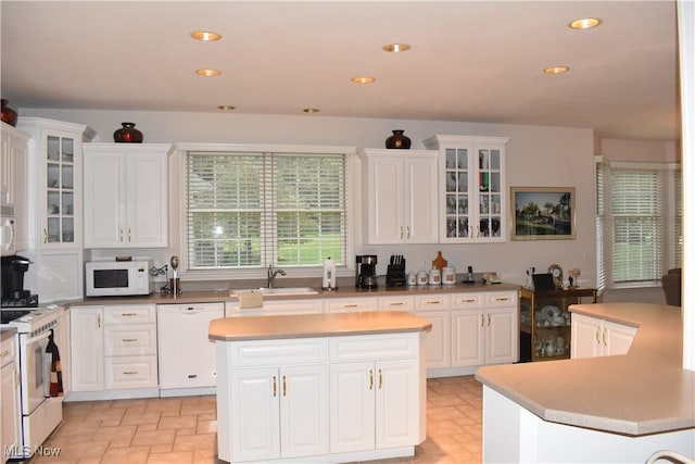 kitchen with white appliances, white cabinets, a kitchen island, glass insert cabinets, and a sink