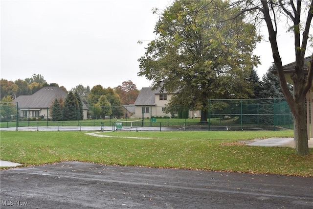 view of home's community with a tennis court, a yard, and fence