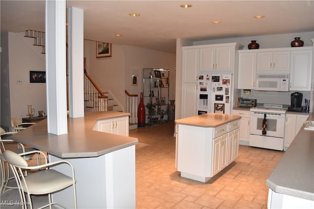 kitchen with white appliances, a kitchen island, white cabinetry, and light countertops