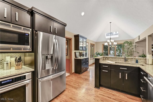 kitchen with decorative light fixtures, light wood finished floors, decorative backsplash, appliances with stainless steel finishes, and light stone countertops