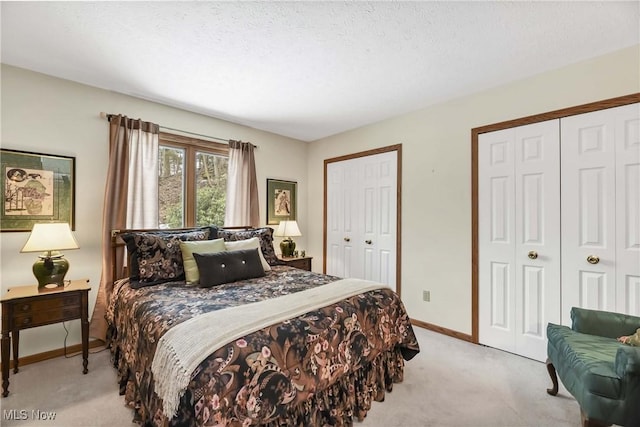 bedroom featuring light colored carpet, a textured ceiling, baseboards, and two closets