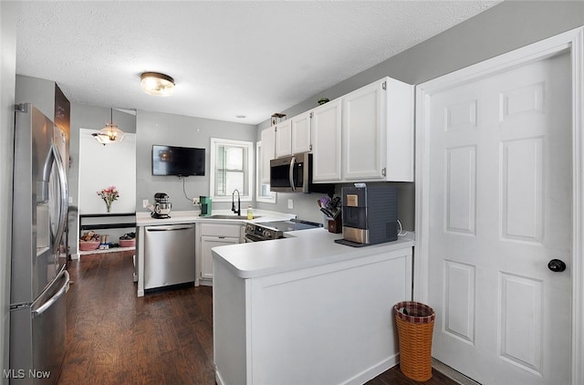 kitchen with dark wood-style flooring, white cabinetry, light countertops, a peninsula, and appliances with stainless steel finishes