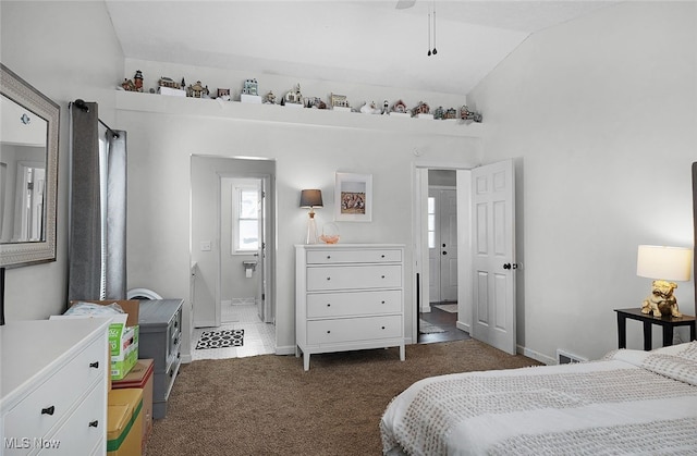 bedroom featuring dark carpet, lofted ceiling, ensuite bathroom, and baseboards