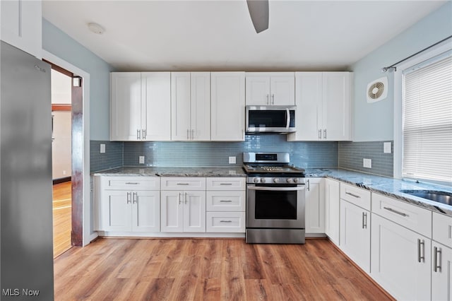 kitchen with white cabinets, light wood-type flooring, stainless steel appliances, and backsplash