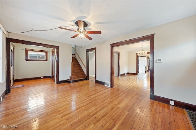 unfurnished room with ceiling fan with notable chandelier, visible vents, baseboards, stairs, and light wood-style floors