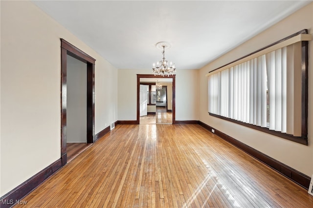 spare room featuring a chandelier, wood-type flooring, visible vents, and baseboards