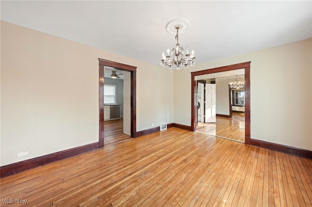 spare room with a notable chandelier, visible vents, baseboards, and hardwood / wood-style floors